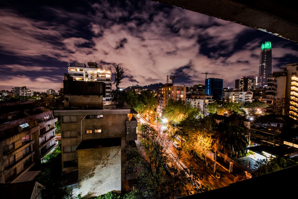 Dramatic night view of Santiago's skyline with lit buildings and cloudy sky.